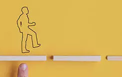  2021/10/blocks-person-ret-245.jpg Silhouette of a man walking on the path made of wooden pegs with other man supporting one of the peg. Conceptual image of teamwork and support. Over yellow background with copy space.
