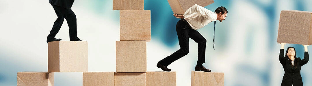  2021/10/blocksbanner_1080x300-e1556028743792.jpg Team of businesspeople build a construction with wood cubes