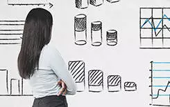  2021/10/charts-woman-245.jpg Businesswoman wearing a skirt and a shirt with high heels looking at infographics with bar charts and diagrams, business icons drawn on a concrete wall. Data representation concept