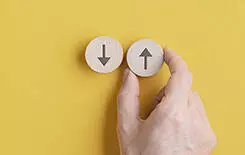  2021/10/direction-245.jpg Wide view image of male hand placing two wooden cut circles with arrows pointing up and down over yellow background.