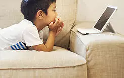  2021/10/family-home-a-boy-lying-on-a-sofa-245.jpg Family home. A boy lying on a sofa watching a digital tablet.