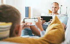  2021/10/father-son-home-products-in-use-245.jpg Father and son playing with tablet and gamepad sitting in living room