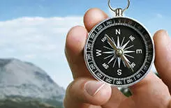  2021/10/landscape-compass-spot.jpg Close up of the hand of a man holding a magnetic compass over a landscape view as he uses it to navigate when exploring or travelling in the countryside