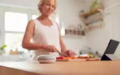  2021/10/woman-kitchen-with-smart-speaker-245.jpg Retired Woman Making Meal In Kitchen With Smart Speaker In Foreground