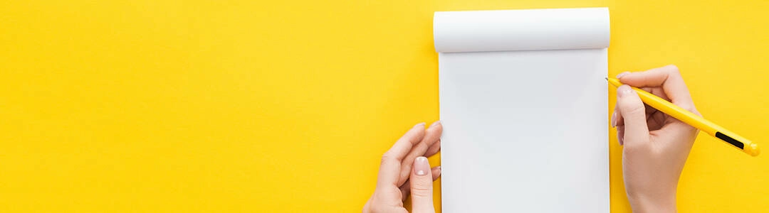  2021/10/writing-1080.jpg partial view person holding pen over blank notebook on yellow background