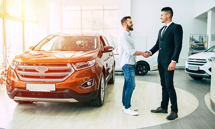 Manager in an auto dealership shakes hands with a young man who is car shopping