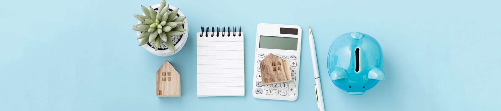 Calculator with house model, notebook and piggy bank, housing finance concept on blue table, top view