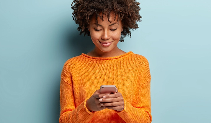 Young woman in an orange sweater holding a smartphone