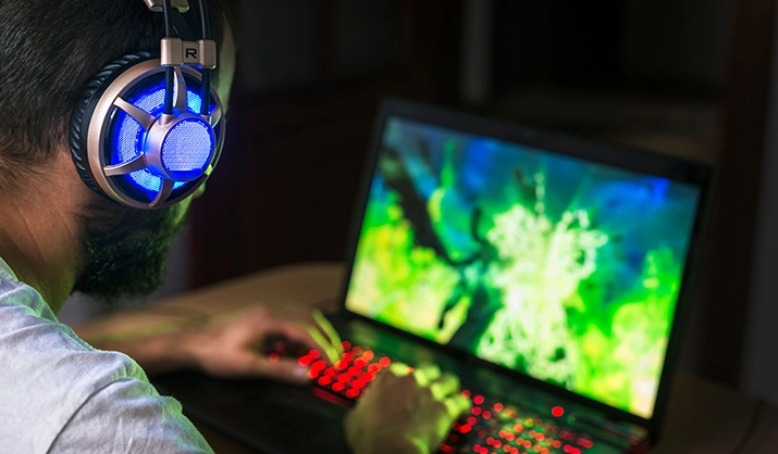 gamer playing video game on laptop wearing headphones