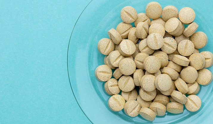 Beige supplement pills in a clear glass bowl on a turquoise background