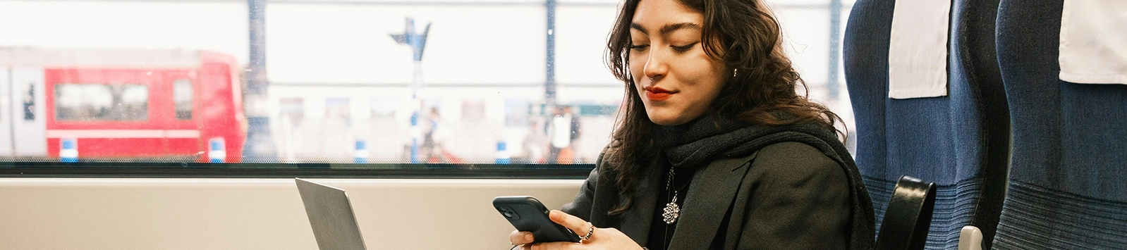 Woman using a mobile phone and a laptop on a train.