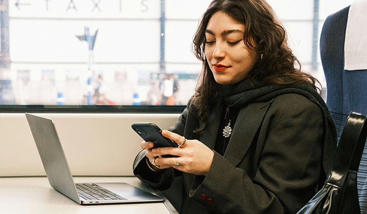 Woman using a mobile phone and a laptop on a train.